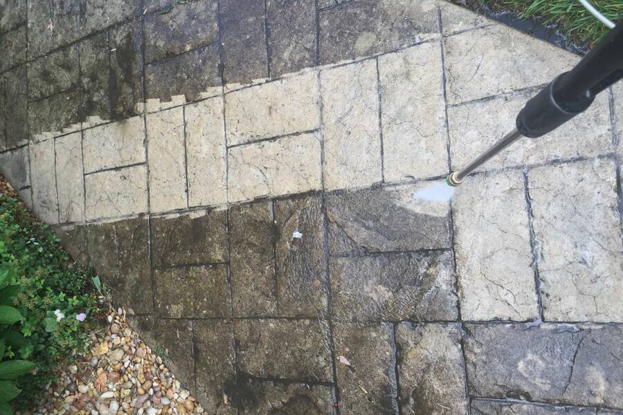 A pressure washer clearing dirt from paving, half of it cleaned